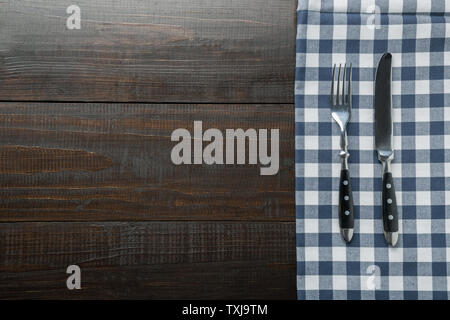 Rustic black silverware with blue checkered towel on brown wooden board. Top view with copy space for your menu or recipe. Cooking food background. Stock Photo