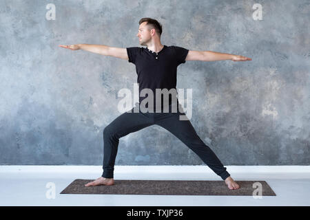 Man practicing yoga in studio doing Warrior 2 pose Stock Photo
