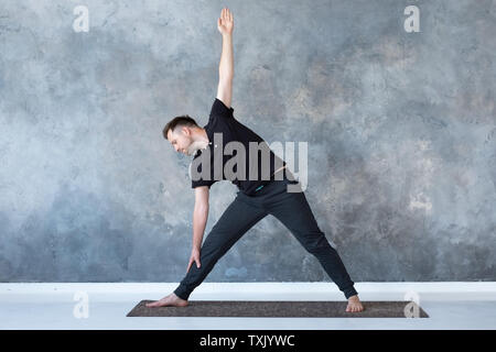 Man beginner practicing yoga doing trikonasana pose. Stock Photo