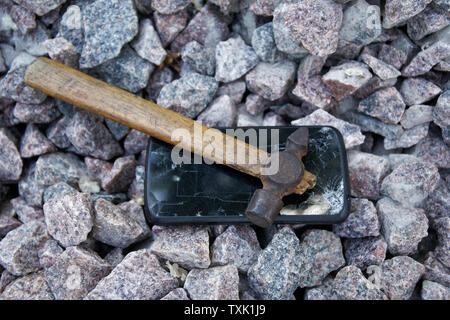Broken glass of smartphone with hammer on gravel stones. Selective focus. Stock Photo