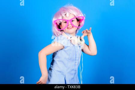 Small girl headphones pink wig dancing. Child using technology for fun. Modern headphones. Energy motion dance. Inspired by music. Little kid listening music. Cute kid with headphones blue background. Stock Photo