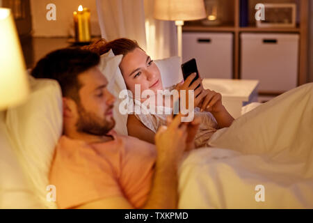 couple using smartphones in bed at night Stock Photo