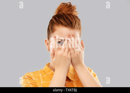 red haired teenage girl looking through fingers Stock Photo