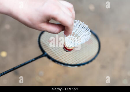 hand holds shuttlecock over badminton racquet on outdoor earth ground Stock Photo