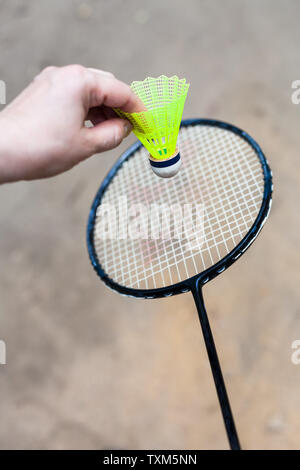 hand holds yellow shuttlecock over badminton racquet on outdoor earth ground Stock Photo