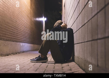 Sad teen sitting in an alleyway all alone at night. Stock Photo