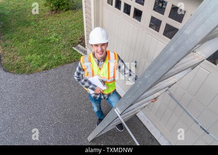 Young male architect standing on a ladder and dressed in safety gear. Stock Photo