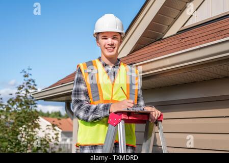 Home inspector standing on a ladder and providing an inspection to the roof of a house. Stock Photo