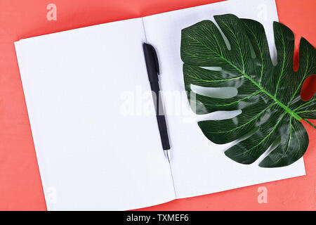 Blank notebook on coral background, tropical leaf. Top view, flat lay. Mockup, copy space. Summer background, travel. Stock Photo