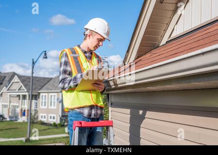 Home inspector standing on a ladder and providing an inspection to the roof of a house. Stock Photo