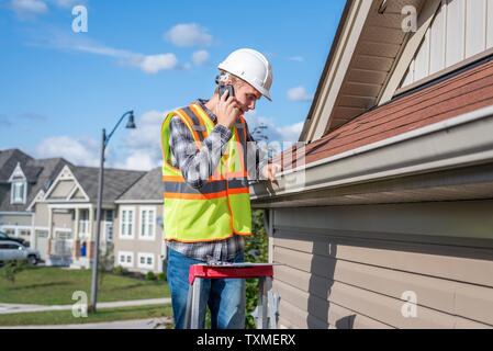 Young architect standing on a ladder and talking on his cellphone. Stock Photo