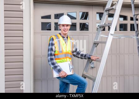 Young male architect standing on a ladder and dressed in safety gear. Stock Photo