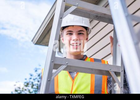 Young male architect standing on a ladder and dressed in safety gear. Stock Photo