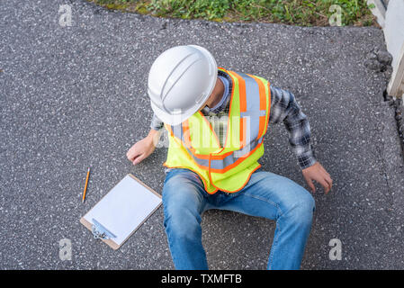 Injured architect sitting on the ground after having fallen off a ladder. Stock Photo