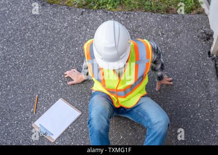 Injured architect sitting on the ground after having fallen off a ladder. Stock Photo