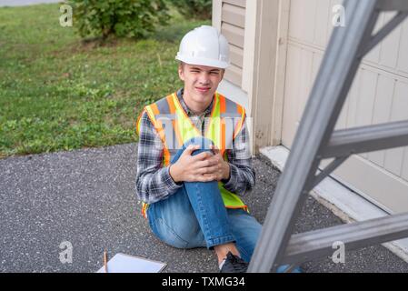 Injured architect sitting on the ground after having fallen off a ladder. Stock Photo