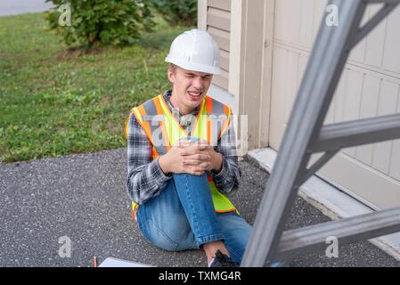 Injured architect sitting on the ground after having fallen off a ladder. Stock Photo