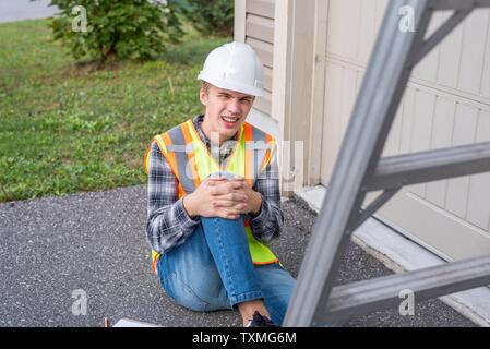 Injured architect sitting on the ground after having fallen off a ladder. Stock Photo