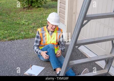 Injured architect sitting on the ground after having fallen off a ladder. Stock Photo
