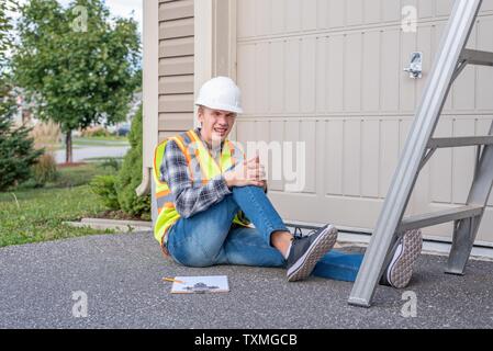 Injured architect sitting on the ground after having fallen off a ladder. Stock Photo