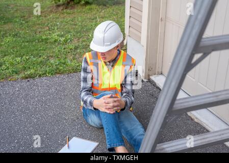 Injured architect sitting on the ground after having fallen off a ladder. Stock Photo
