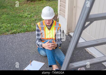 Injured architect sitting on the ground after having fallen off a ladder. Stock Photo