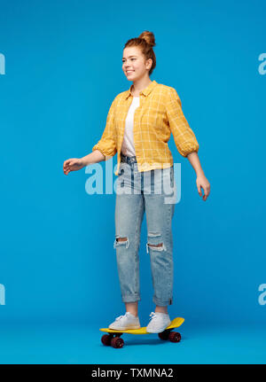 red haired teenage girl riding on short skateboard Stock Photo