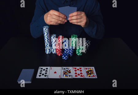 Close up of guy poker player hands holding cards and betting chips at the casino table. Gambling tournament winner success concept over black backgrou Stock Photo