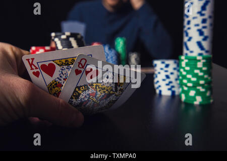 Close up of young man poker player looking cautious at his playing cards. Betting chips on the casino table. Gambling tournament winner success concep Stock Photo