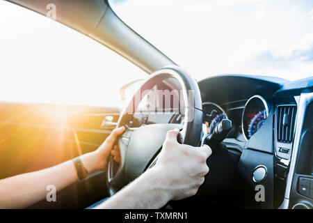 Driving a car, shot from the passenger seat. Male's hands on steering wheel of a modern vehicle on the road, shot against the sun Stock Photo