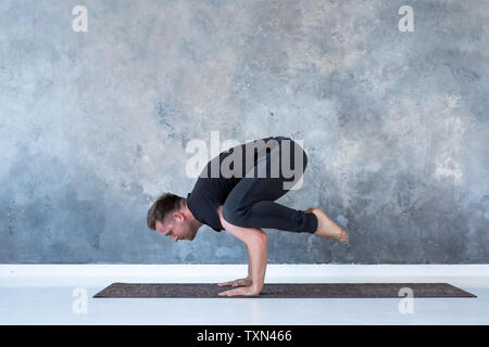 Sporty young man working out, doing handstand yoga asana, Crow Pose or Bakasana Stock Photo