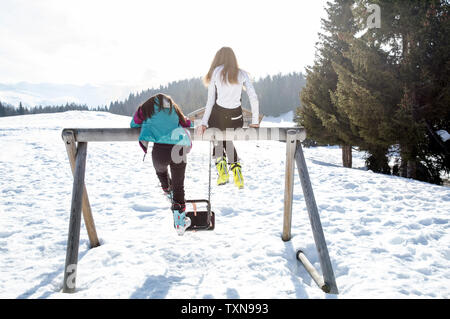 Two teenage girl skiers sitting on top of swing in snow covered landscape, rear view, Tyrol, Styria, Austria Stock Photo