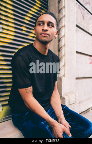 Young man waiting on window ledge of building Stock Photo