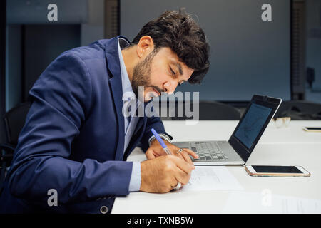 Businessman writing notes and using laptop in office Stock Photo