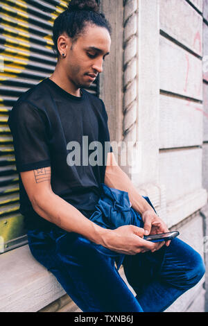 Young man using smartphone on window ledge of building Stock Photo