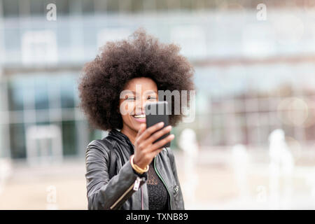 Young woman with afro hair taking smartphone selfie on city concourse Stock Photo