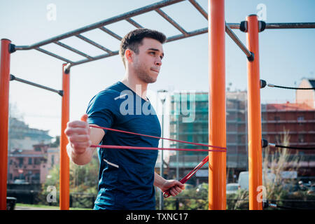 Calisthenics at outdoor gym, young man stretching arms on exercise equipment Stock Photo