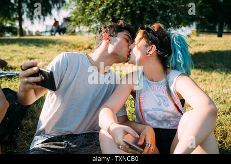 Couple kissing, using smartphone in park Stock Photo