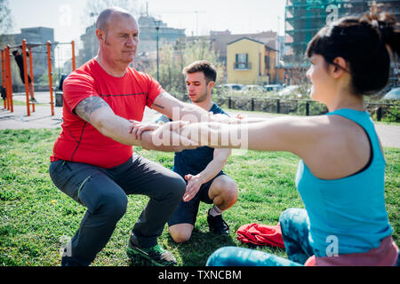 Calisthenics class at outdoor gym, instructor supporting man and woman practicing yoga Stock Photo