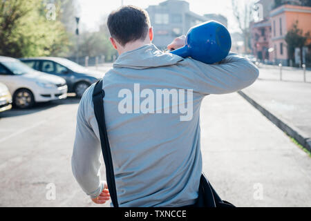 Calisthenics in park, young man carrying kettlebell over his shoulder, rear view Stock Photo