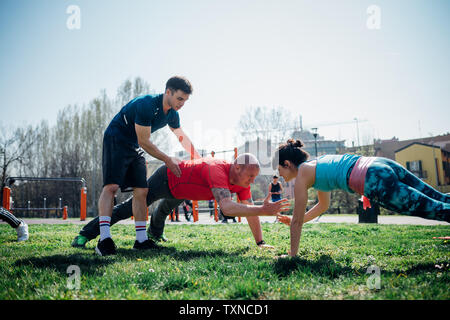 Calisthenics class at outdoor gym, instructor supporting man and woman practicing yoga Stock Photo