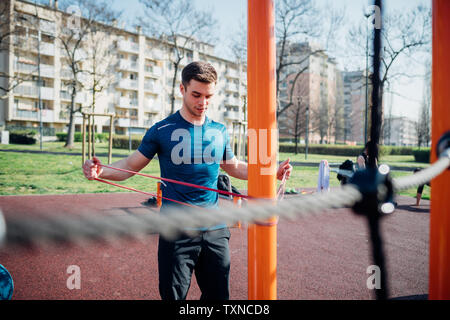 Calisthenics at outdoor gym, young man stretching arms on exercise equipment Stock Photo