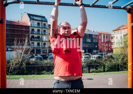 Calisthenics at outdoor gym, mature man doing pull up on exercise equipment Stock Photo