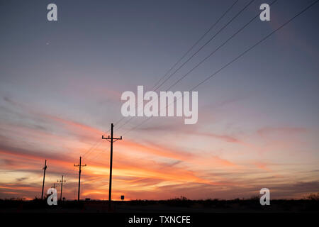 Sunset over highway lined with telephone poles Stock Photo