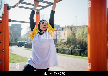 Calisthenics class at outdoor gym, young woman hanging from exercise equipment Stock Photo