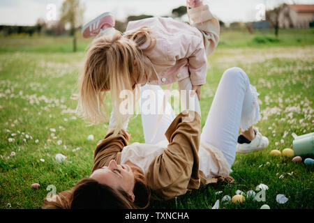 Mother lying on back holding up daughter in wildflower field after easter egg hunt, Arezzo, Tuscany, Italy Stock Photo
