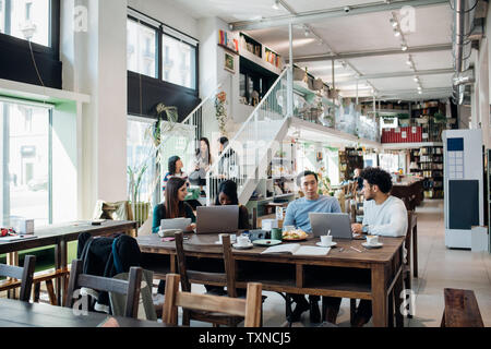 Young businesswomen and businessmen remote working having meeting at cafe table Stock Photo