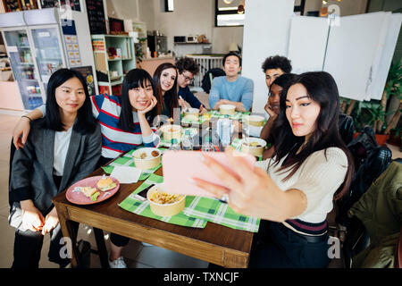 Young male and female business team having working lunch at cafe table, taking smartphone selfie Stock Photo