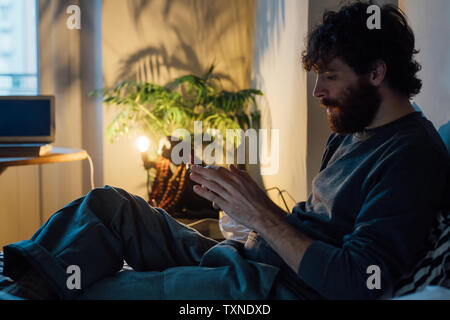 Bearded young man using smartphone in bed Stock Photo