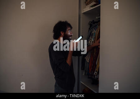 Bearded young man talking on smartphone in front of wardrobe Stock Photo
